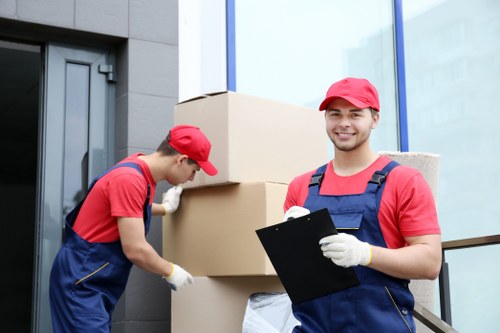 Piano movers carefully handling an upright piano in a Brent home
